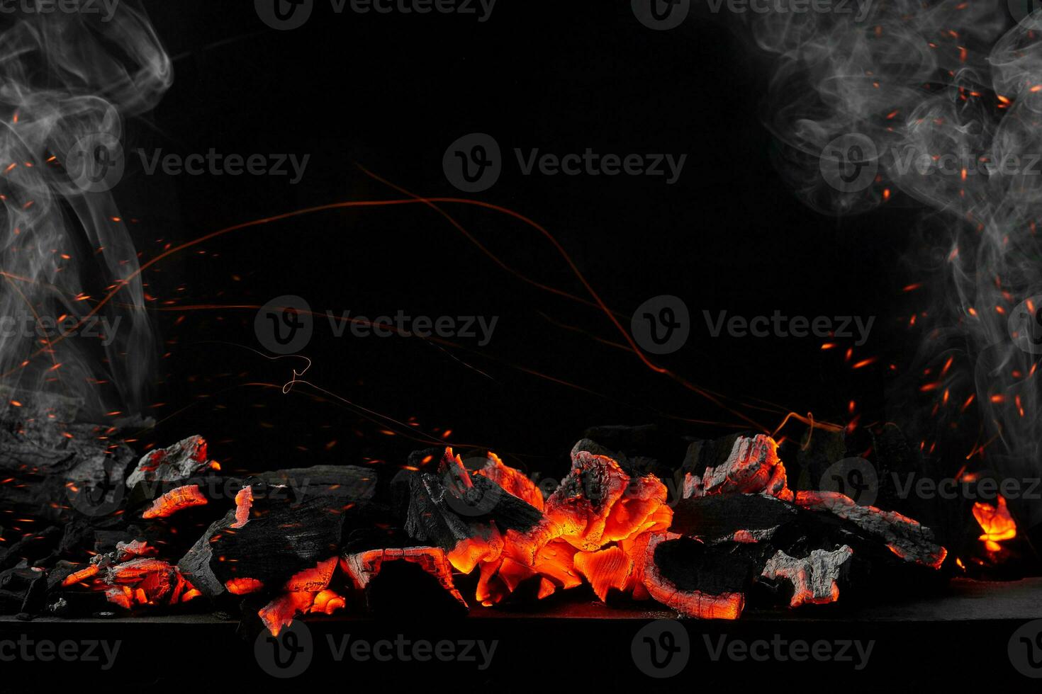Hot burning coals on barbecue tray on black background with sparks and white smoke photo