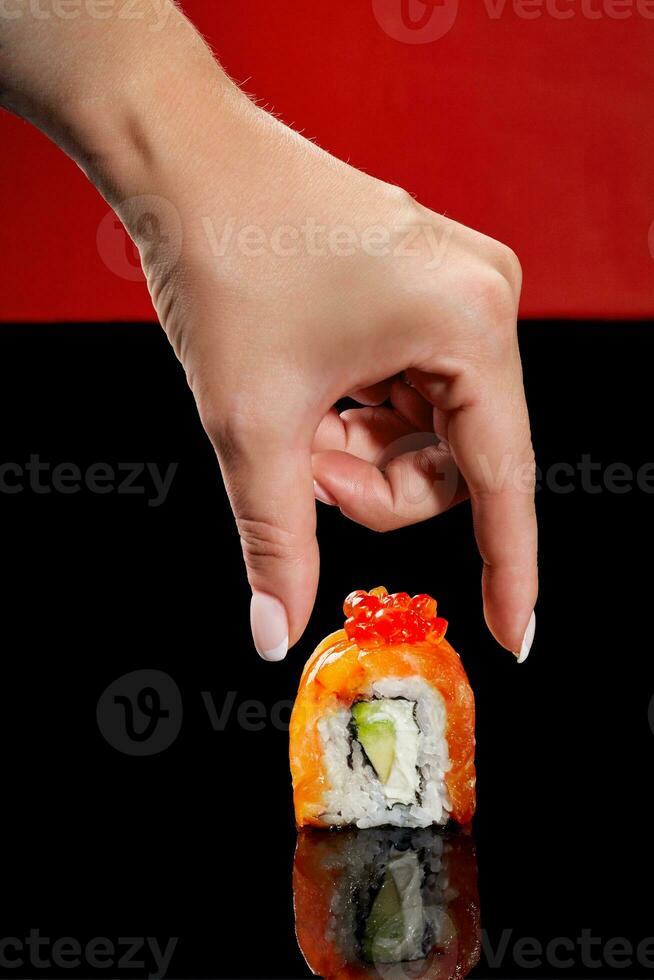 Female hand reaching out to Philadelphia sushi roll with salmon, cream cheese, avocado and red caviar photo