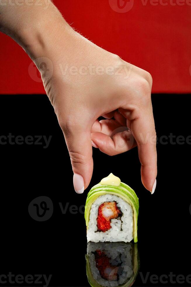 hembra mano tomando Sushi rodar con camarón, volador pescado hueva, aguacate y japonés mayonesa foto