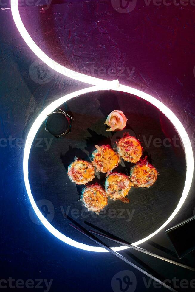 Sushi rolls with melted cheese and bonito flakes on black background with LED strip lighting photo