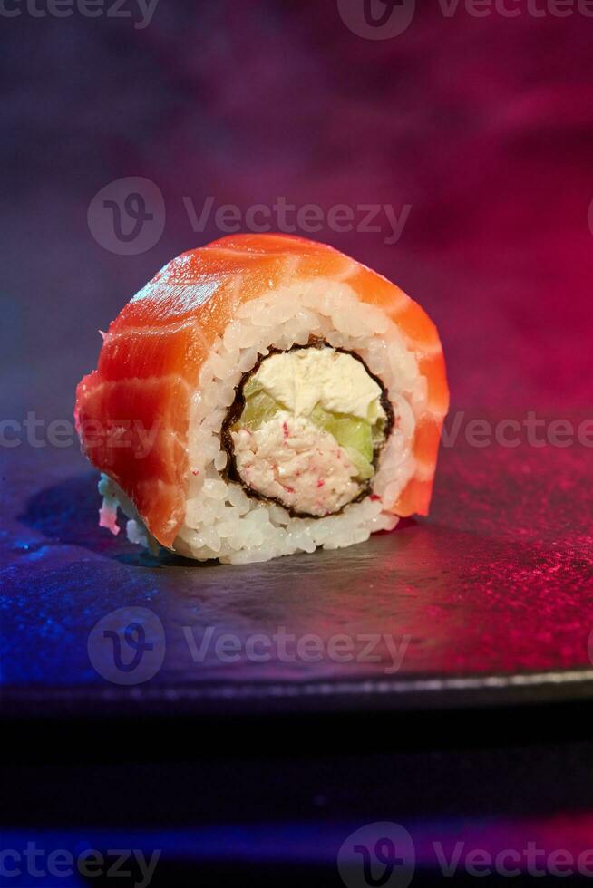 Closeup of one Philadelphia sushi roll with salmon on bright multicolored background of neon lighting photo