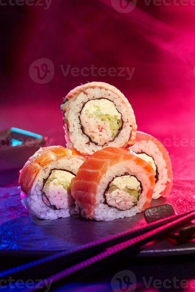 Sushi rolls served at party against multicolored background of neon lighting photo