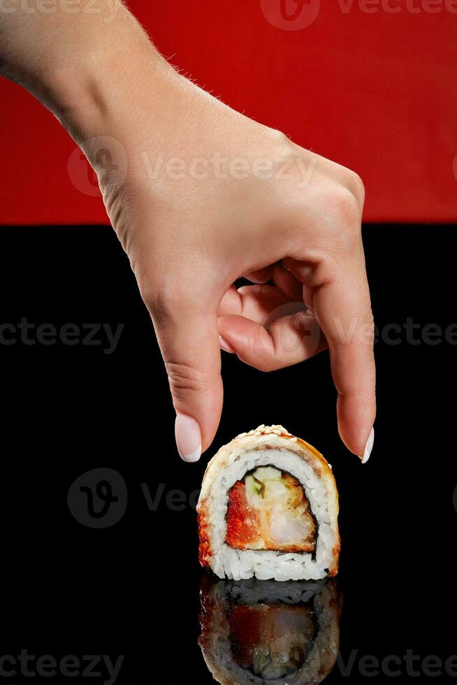 Female hand reaching out to roll with shrimp, tobiko, cucumber, eel and sesame photo