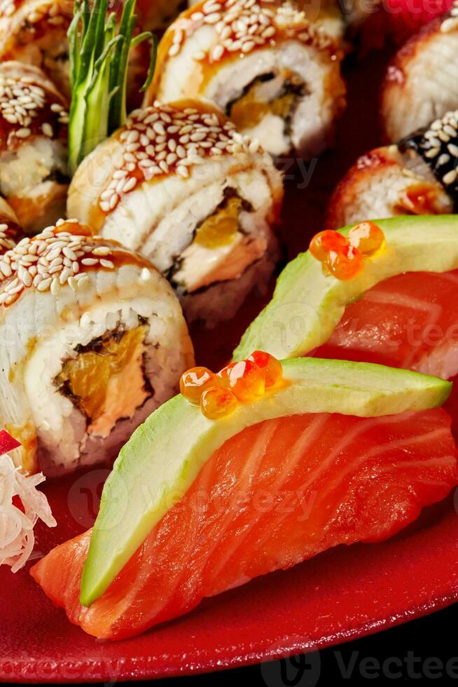 Closeup of nigiri sushi with salmon, avocado, red caviar and unagi rolls with eel, cream cheese and orange on red plate photo