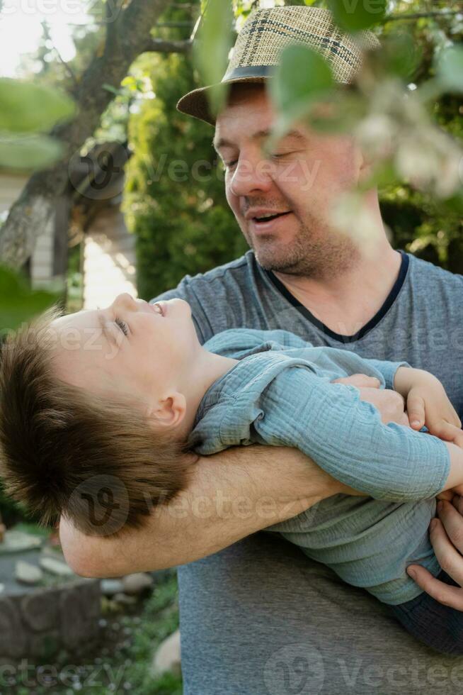 Dad holds happy toddler son in his arms in spring garden. Father day, togetherness concept. photo