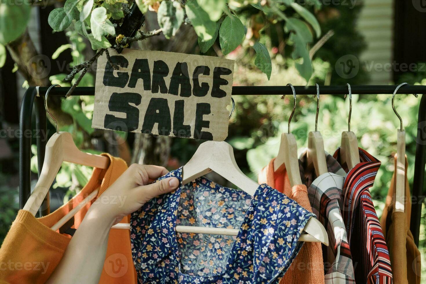 Garage sale. Female hands picking out used apparel hanging on rack. photo