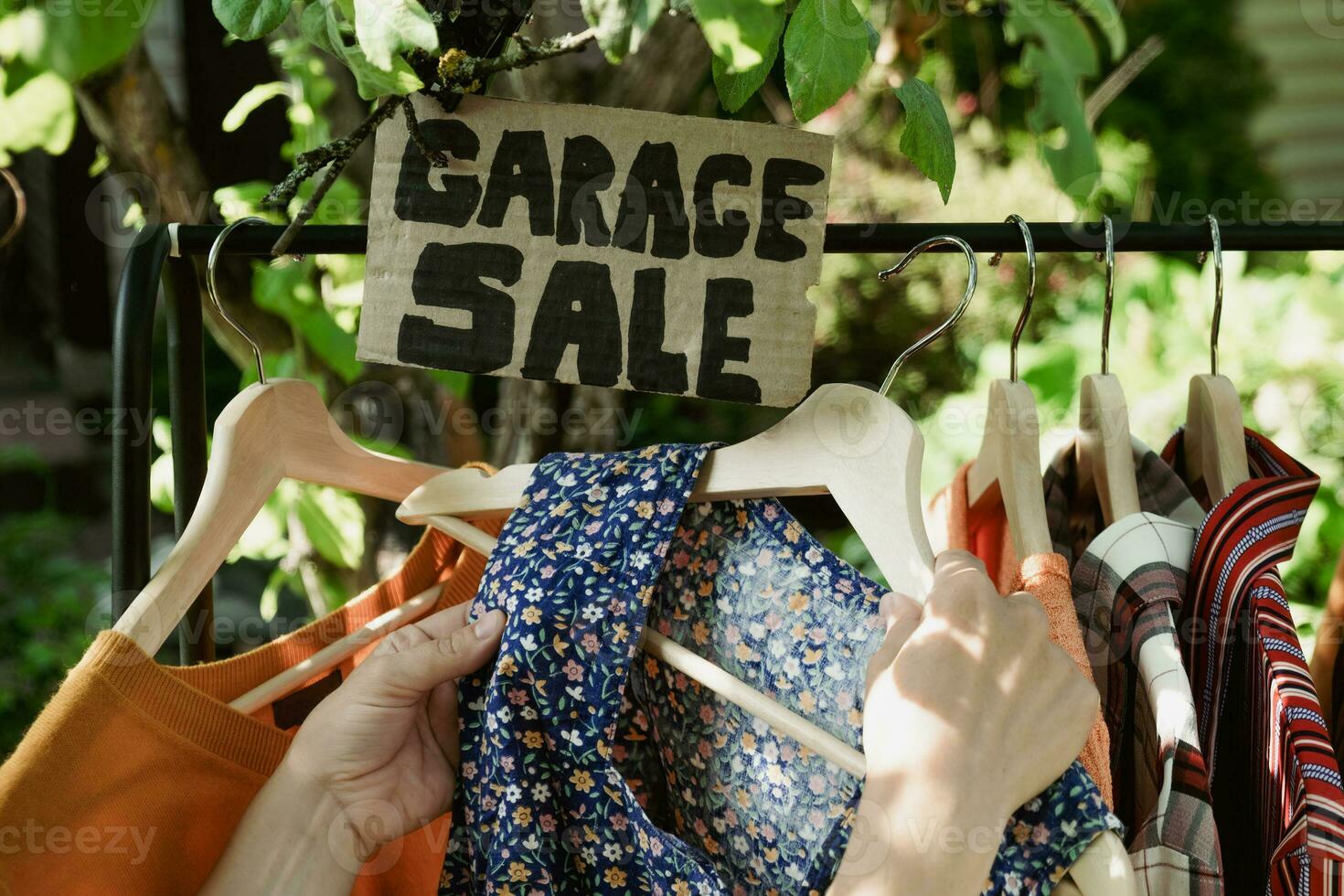 Garage sale. Female hands picking out used apparel hanging on rack. photo