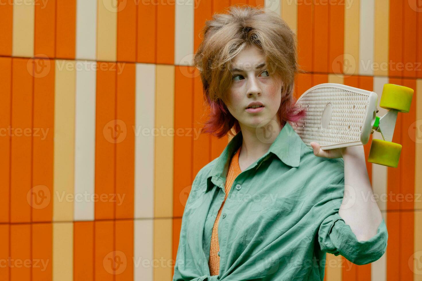 Beautiful skater young woman with skateboard against bright wall. photo