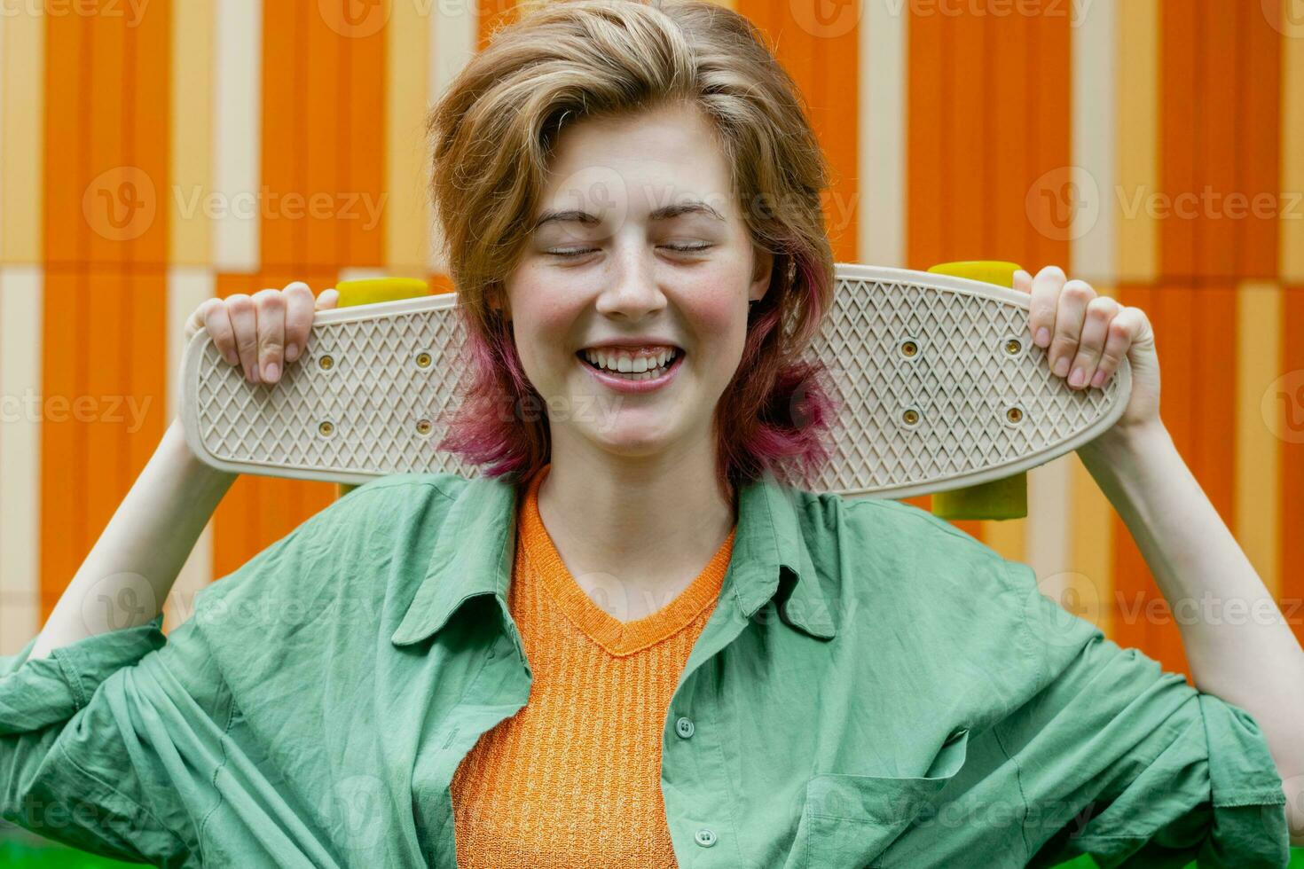 Skater girl smiling holding mini plastic board against colourful urban wall. photo