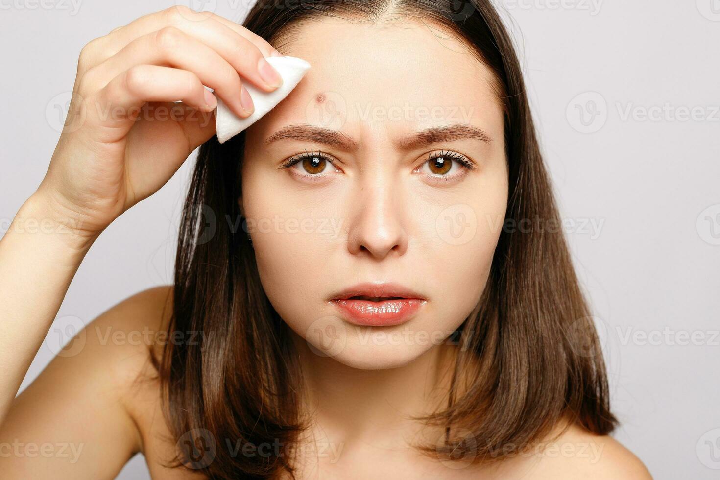 Portrait of young attractive woman touching her face and looking for acne photo