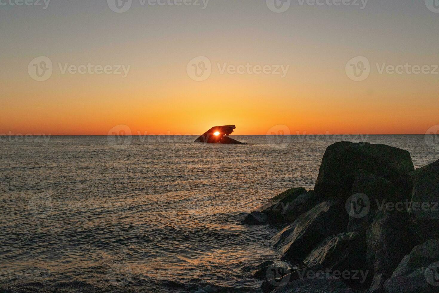 The sunken ship of Cape May New Jersey during sunset. The sun lining up perfectly with hull to look like a glowing eye. The sky has beautiful colors of orange almost like it is on fire. photo