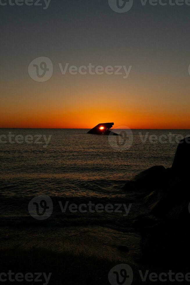 The sunken ship of Cape May New Jersey during sunset. The sun lining up perfectly with hull to look like a glowing eye. The sky has beautiful colors of orange almost like it is on fire. photo