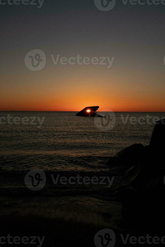 The sunken ship of Cape May New Jersey during sunset. The sun lining up perfectly with hull to look like a glowing eye. The sky has beautiful colors of orange almost like it is on fire. photo