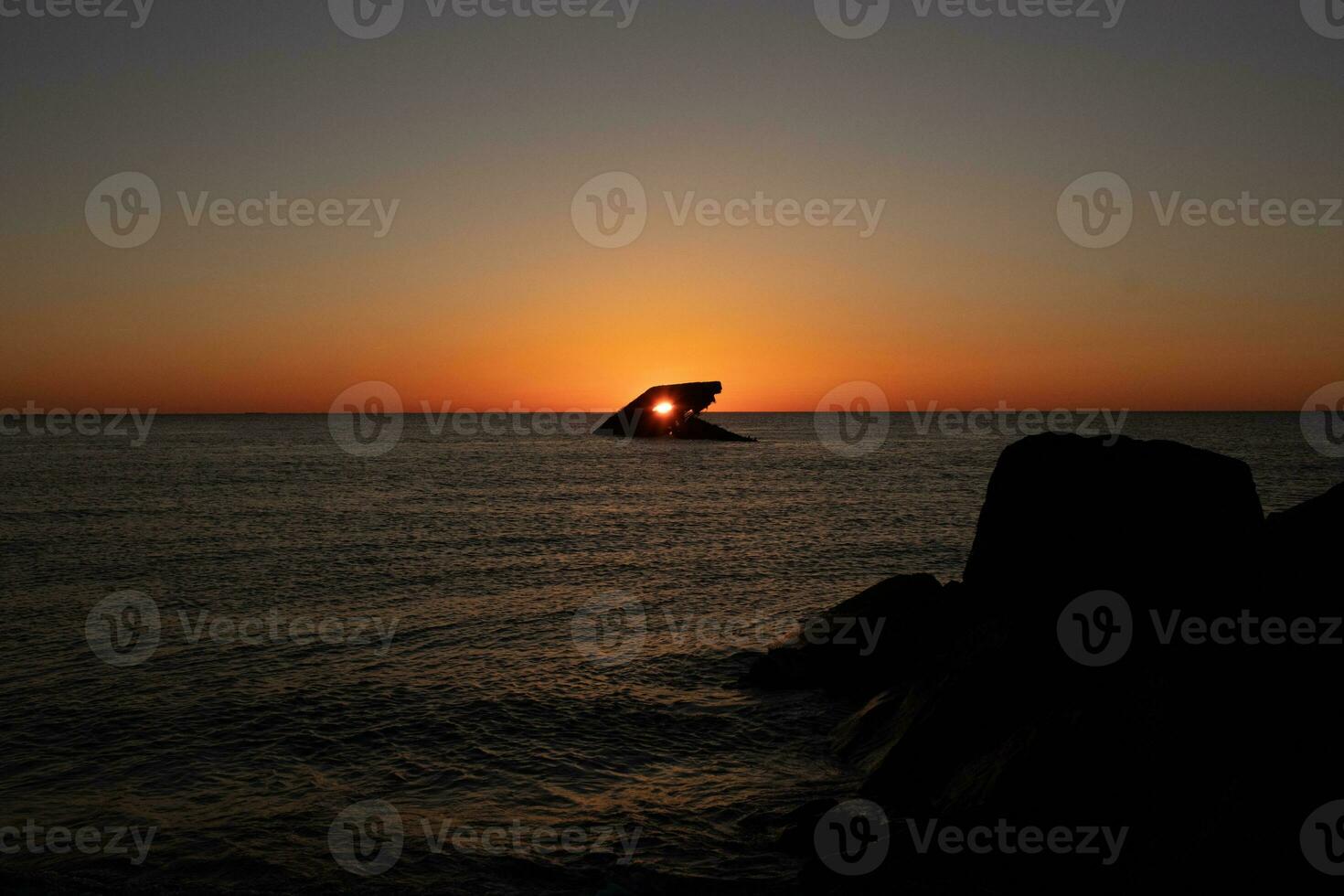 The sunken ship of Cape May New Jersey during sunset. The sun lining up perfectly with hull to look like a glowing eye. The sky has beautiful colors of orange almost like it is on fire. photo