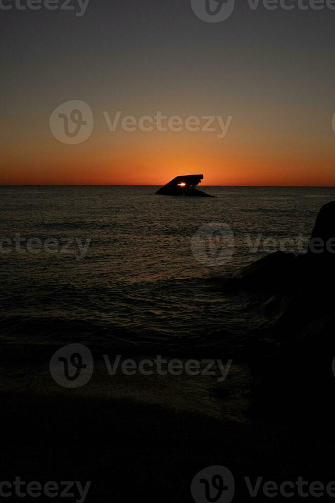 This is the beautiful image of the sunken ship of Cape May New Jersey during sunset. The sky has beautiful colors of orange almost like it is on fire. The fiery shades reflecting off the water. photo
