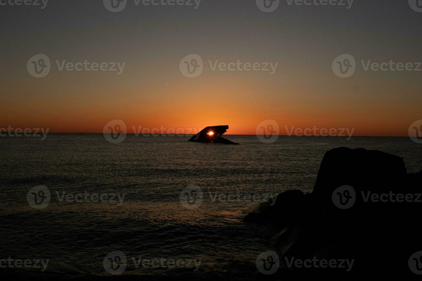 The sunken ship of Cape May New Jersey during sunset. The sun lining up perfectly with hull to look like a glowing eye. The sky has beautiful colors of orange almost like it is on fire. photo