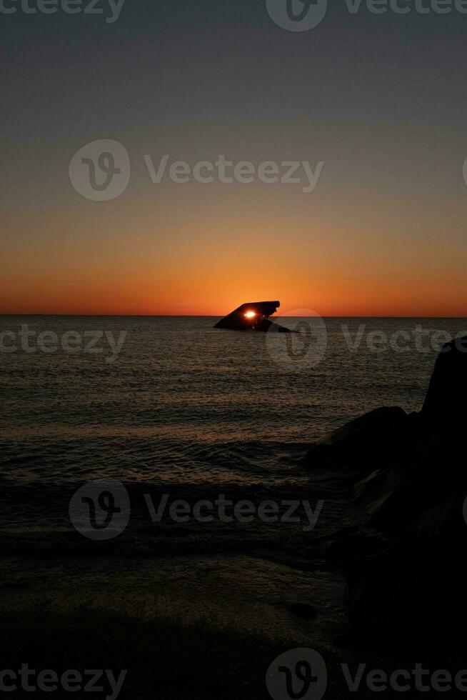 The sunken ship of Cape May New Jersey during sunset. The sun lining up perfectly with hull to look like a glowing eye. The sky has beautiful colors of orange almost like it is on fire. photo