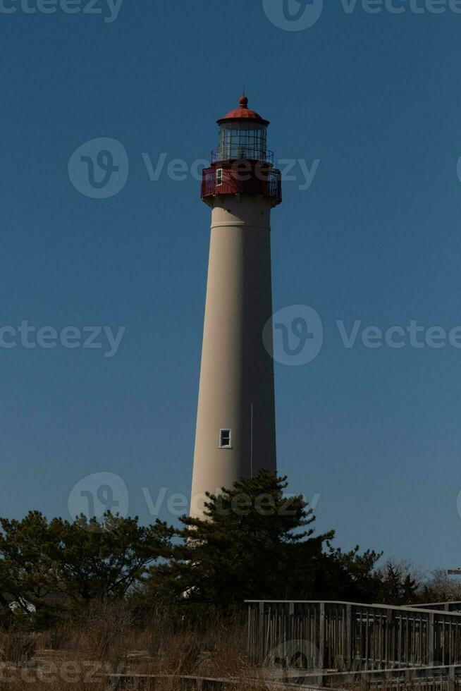 This is Cape May point lighthouse seen from the beach. The tall white structure with red metal serves as a beacon of safety. photo