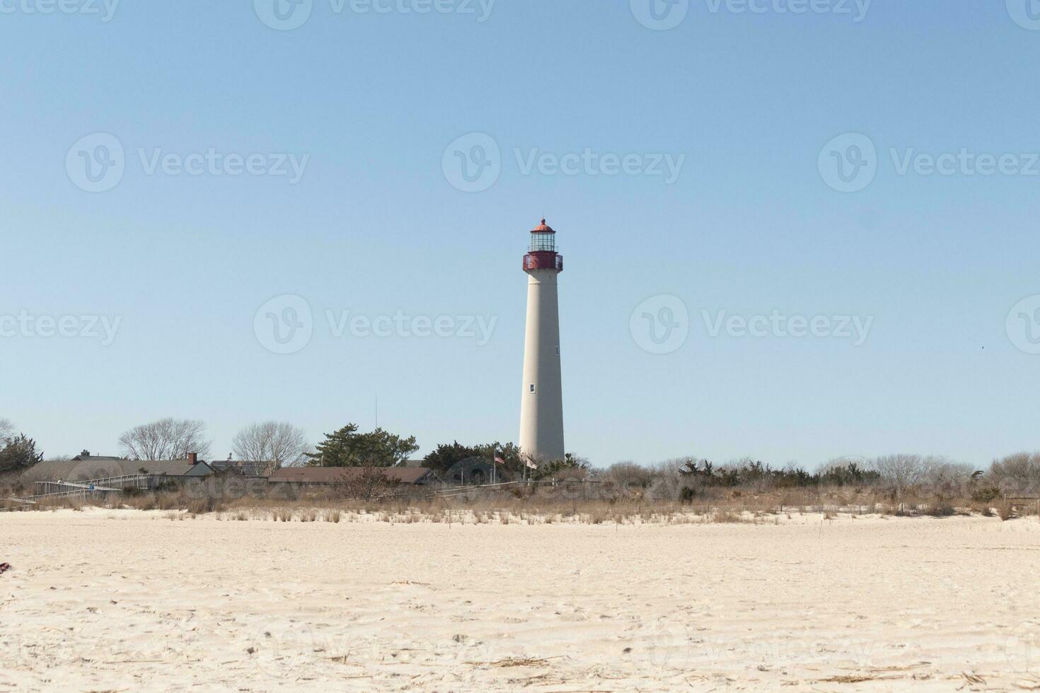 This is Cape May point lighthouse seen from the beach. The tall white structure with red metal serves as a beacon of safety. photo