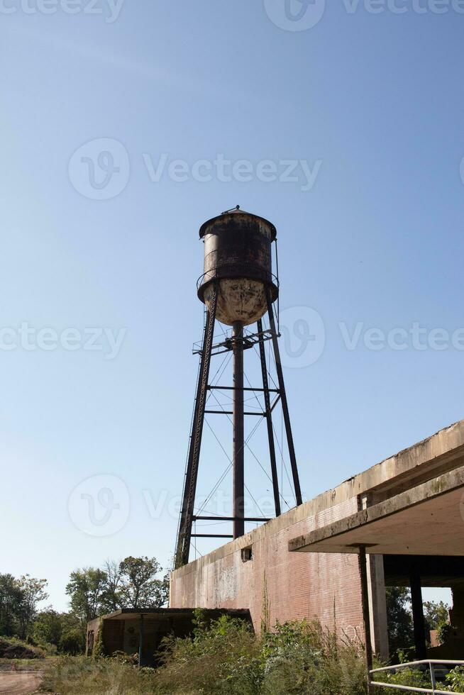 A beautiful water tower is set around an abandoned area. This rusty metal structure stands tall against a blue sky. photo
