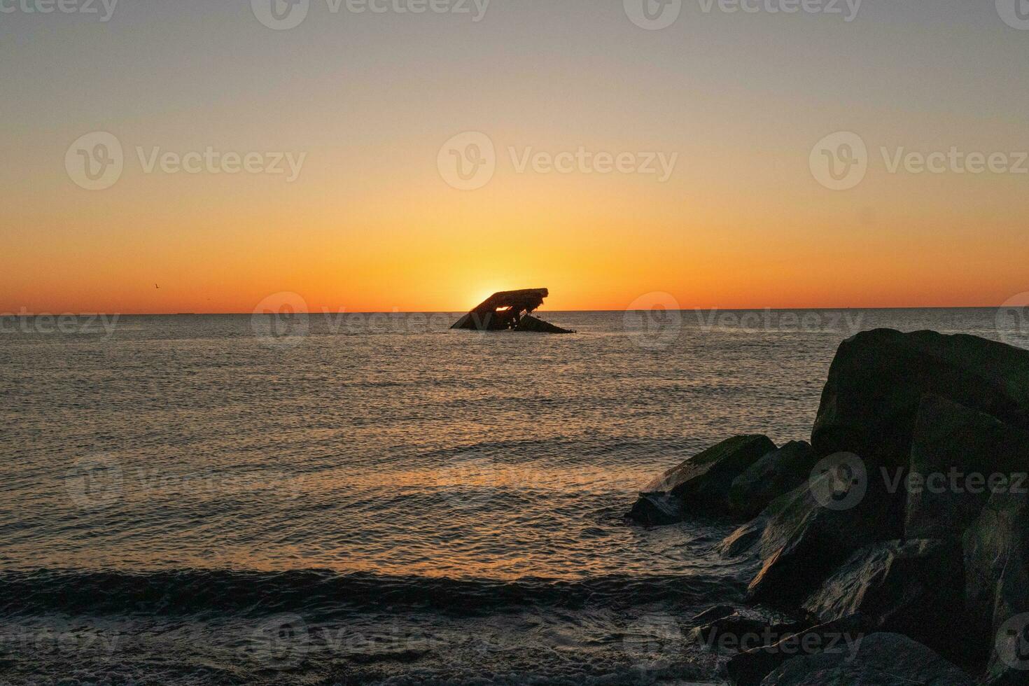 Sunset beach in Cape May New Jersey where you can get a great view of the sun going down across the ocean and the bay. The reflection of the sun on the water with the sunken ship looks so beautiful. photo
