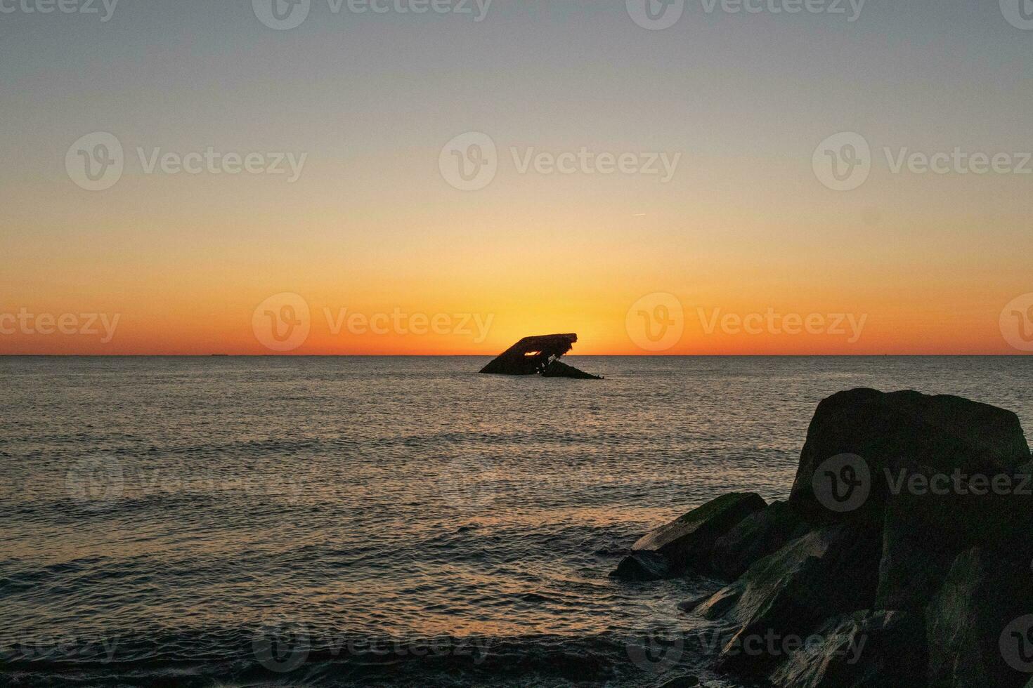Sunset beach in Cape May New Jersey where you can get a great view of the sun going down across the ocean and the bay. The reflection of the sun on the water with the sunken ship looks so beautiful. photo