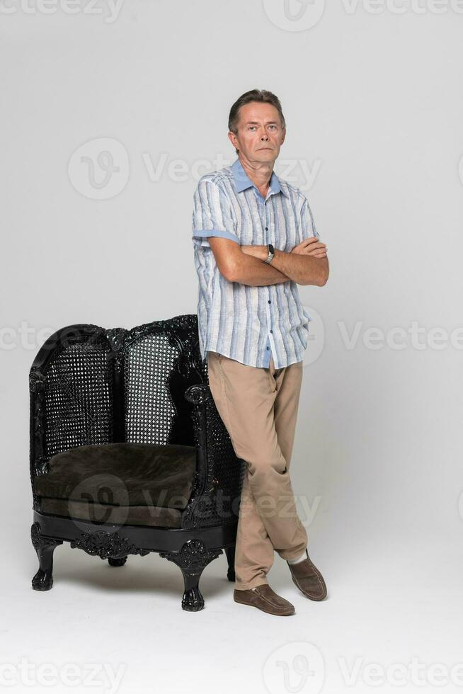 Senior stands near an armchair and pensive, dreamy photo