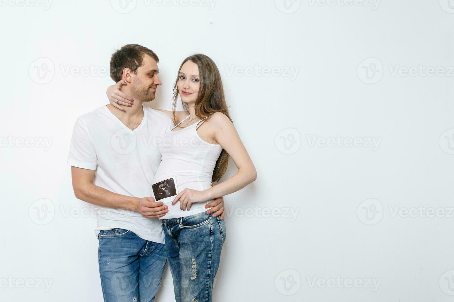 Young married couple embraces standing near the white wall. photo