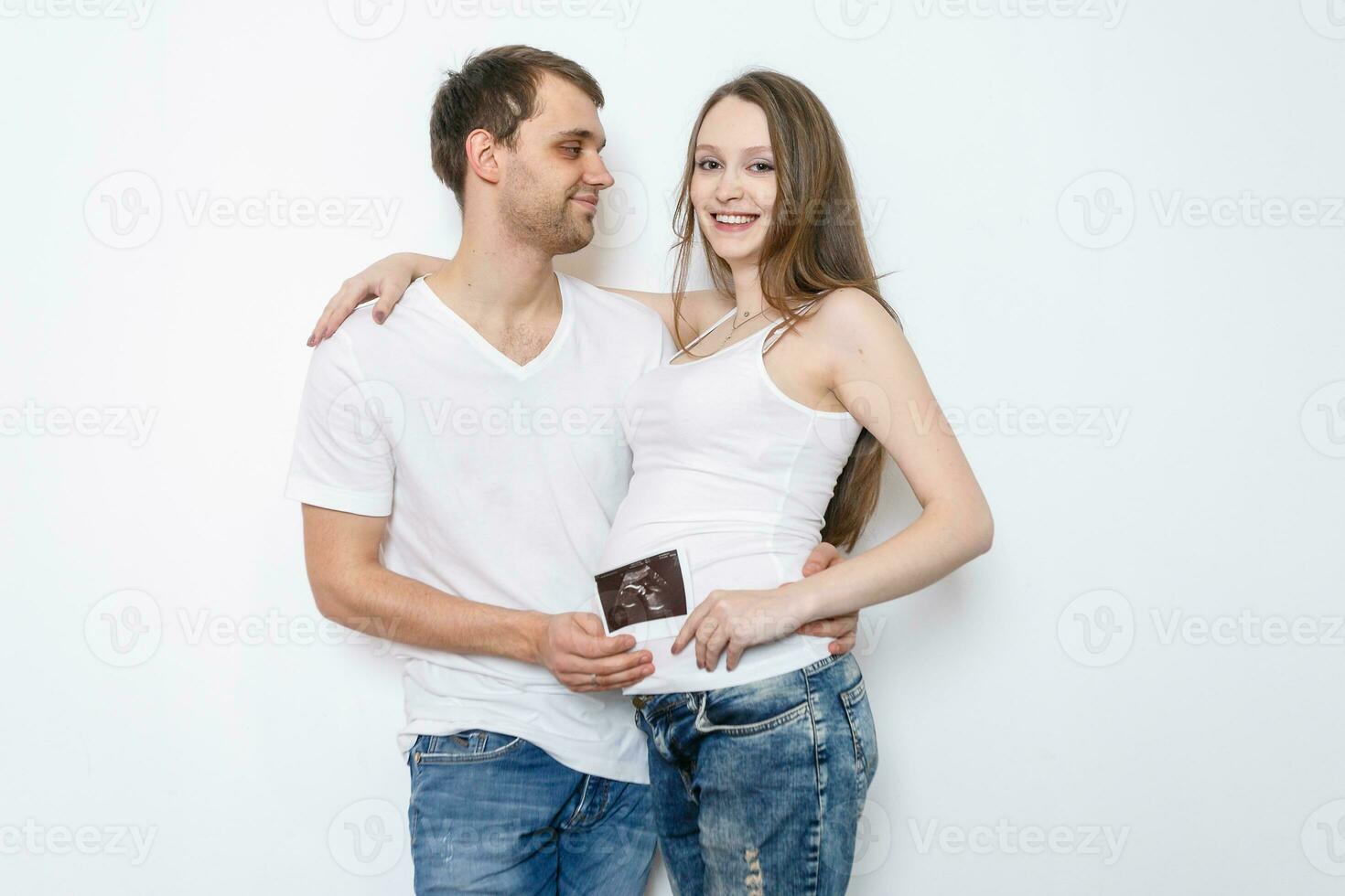 Young married couple embraces standing near the white wall. photo