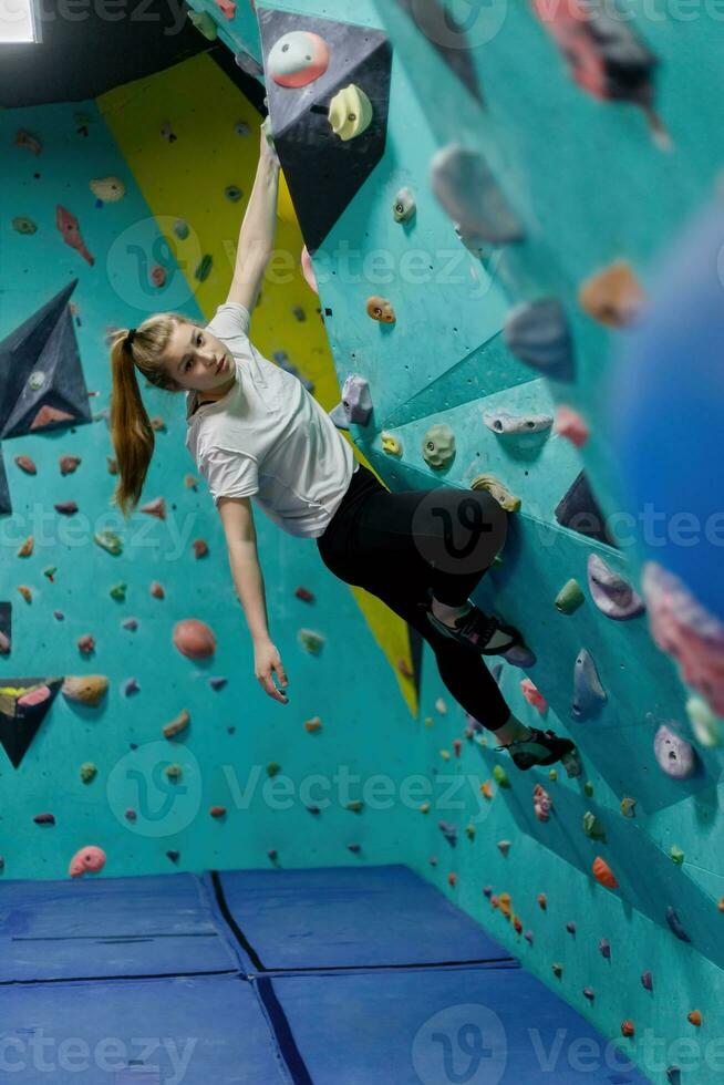 Young woman climbing up on practice wall in gym photo