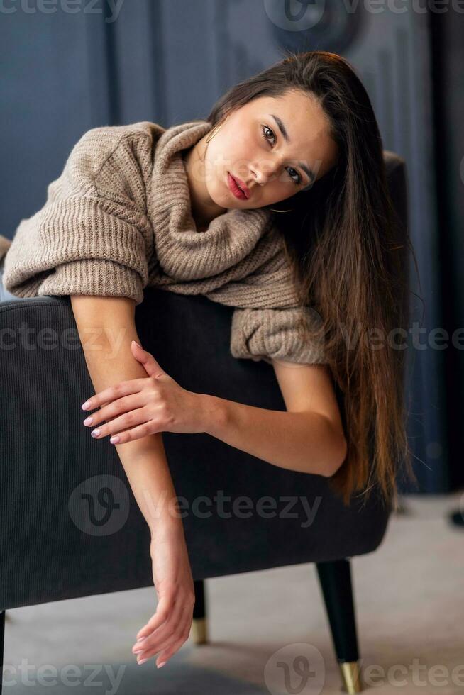 A beautiful young girl is sitting on the back of a chair. photo