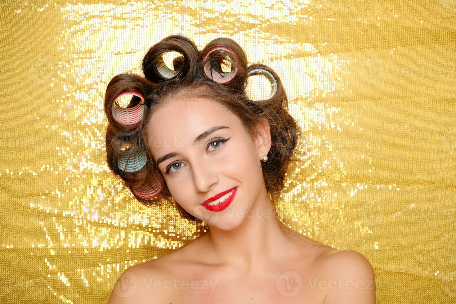 Beautiful girl in hair curlers isolated on gold photo