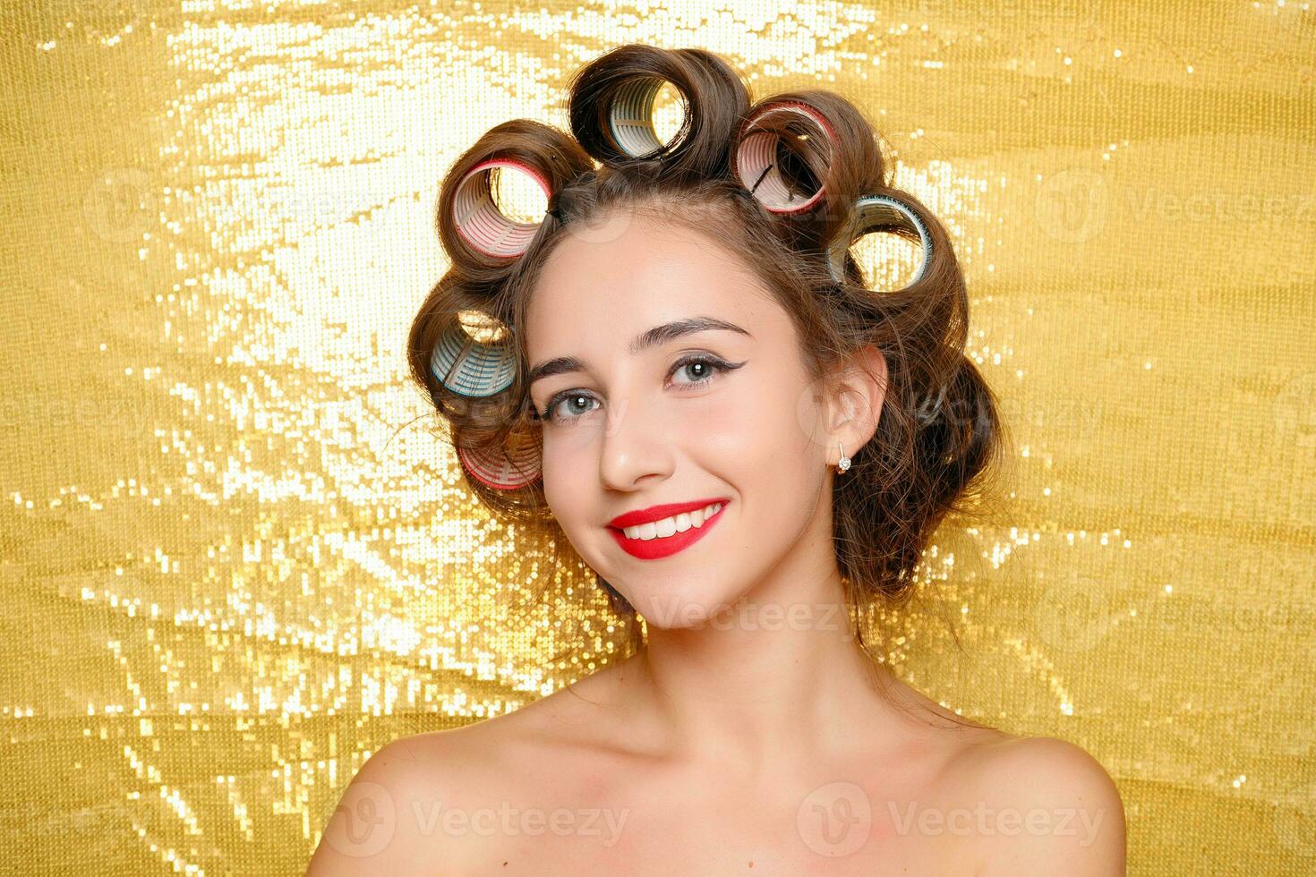 Beautiful girl in hair curlers isolated on gold photo