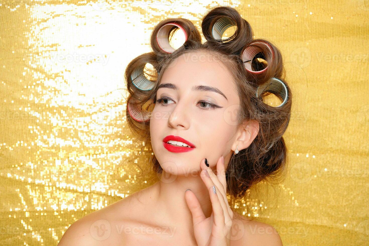 Beautiful girl in hair curlers isolated on gold photo