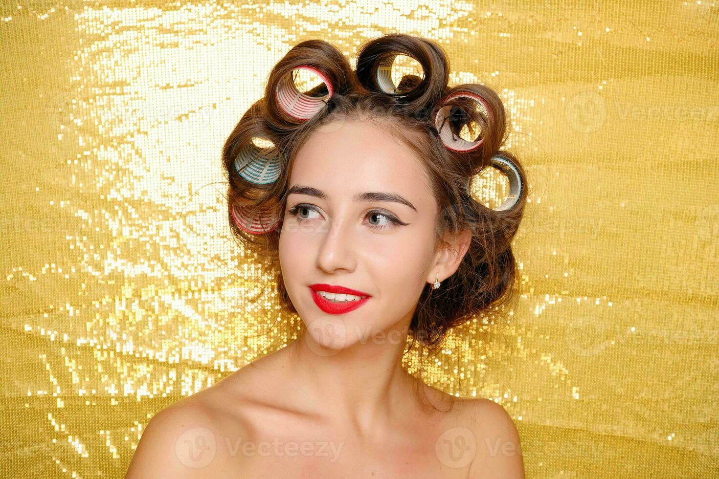 Beautiful girl in hair curlers isolated on gold photo