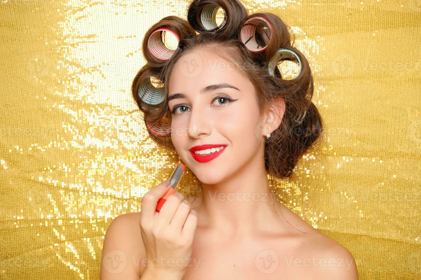 Beautiful girl in hair curlers isolated on gold photo