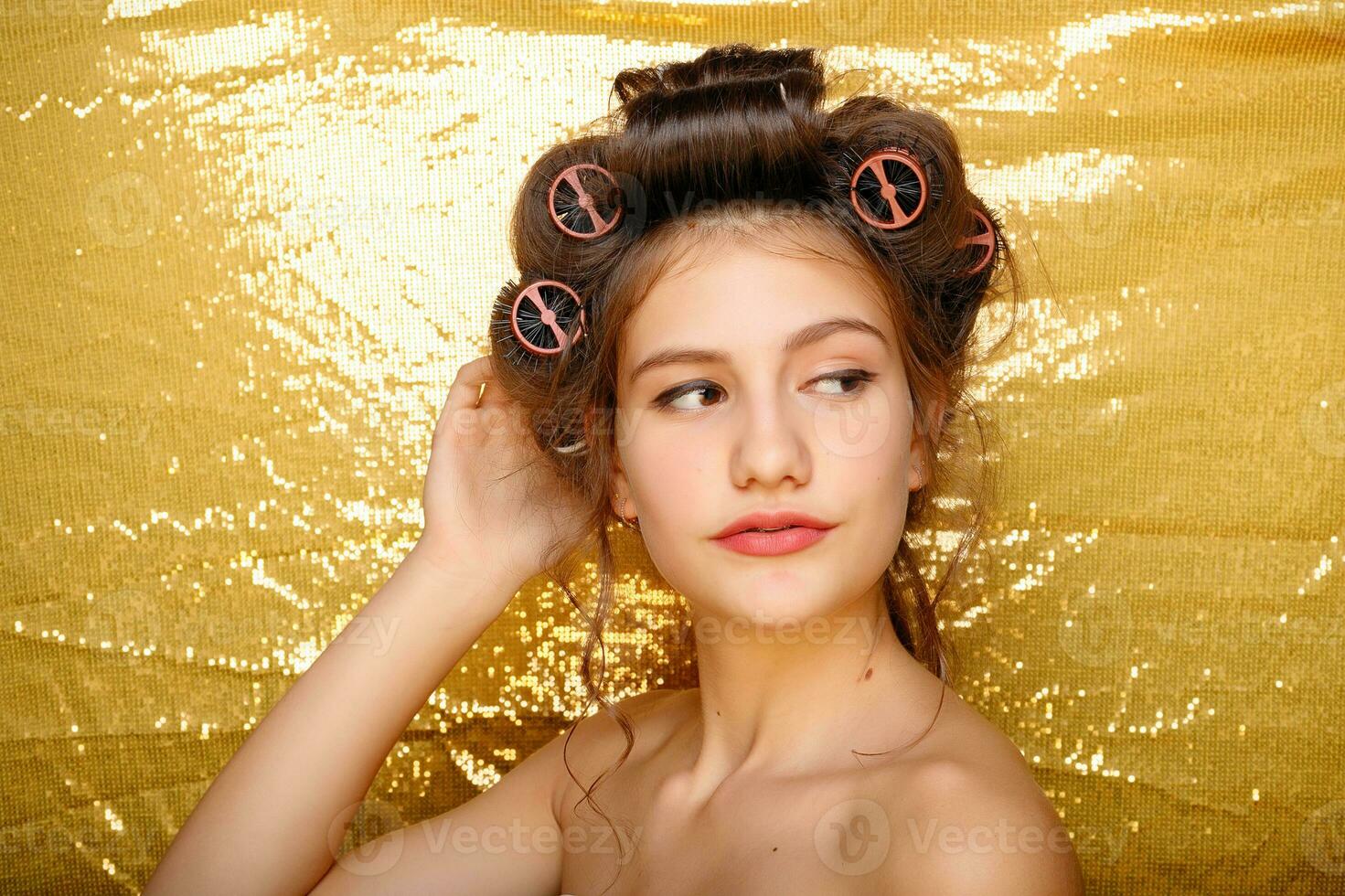 Beautiful girl in hair curlers isolated on gold photo