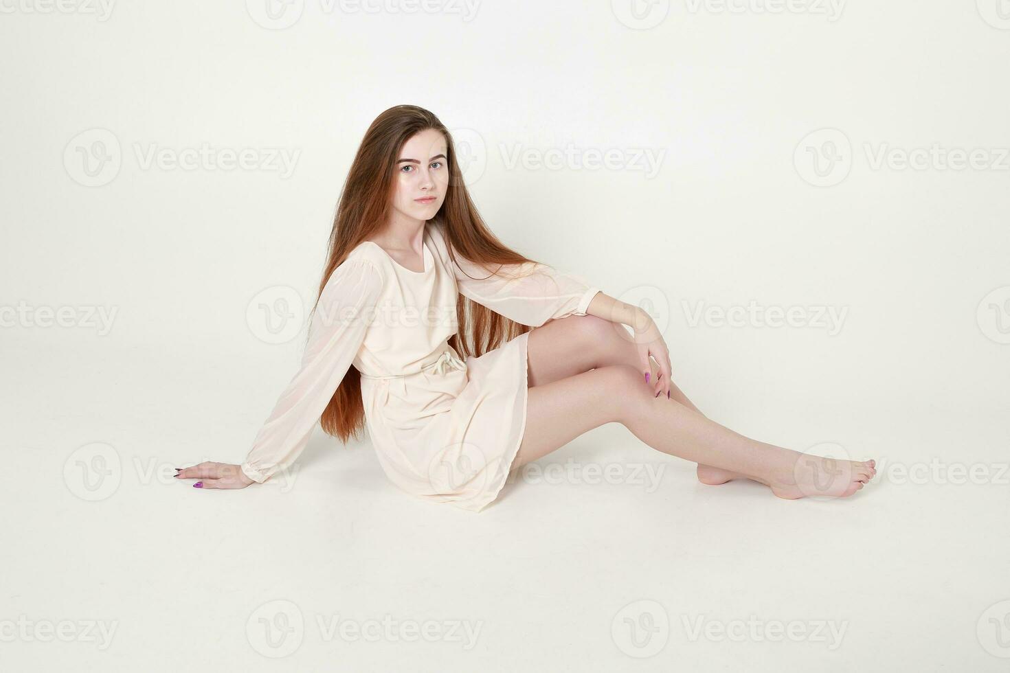 Beautiful tender young girl in a white long dress and with long hair sits photo