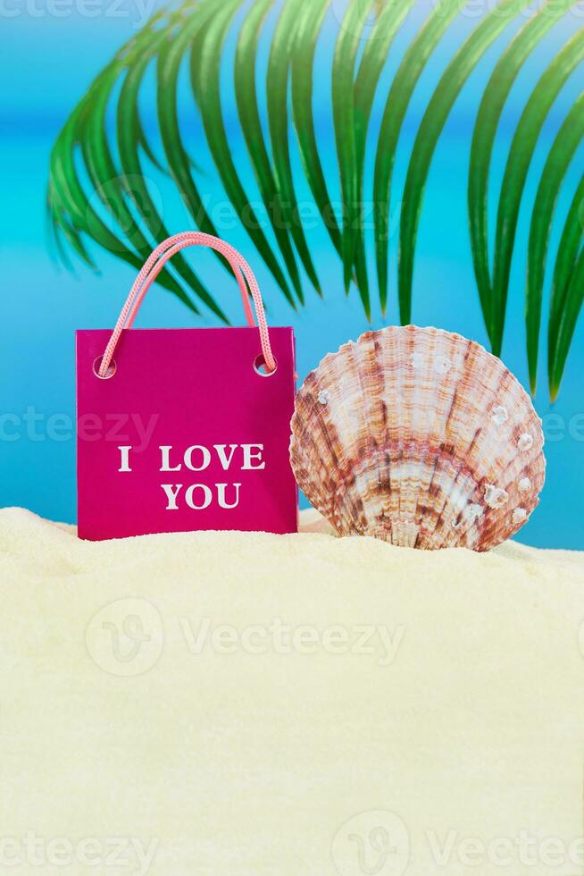 Pink package with i love you and conch shell on sand of beach with palm tree, sea. Valentine's Day, birthday, March 8th, sale. Copy space photo