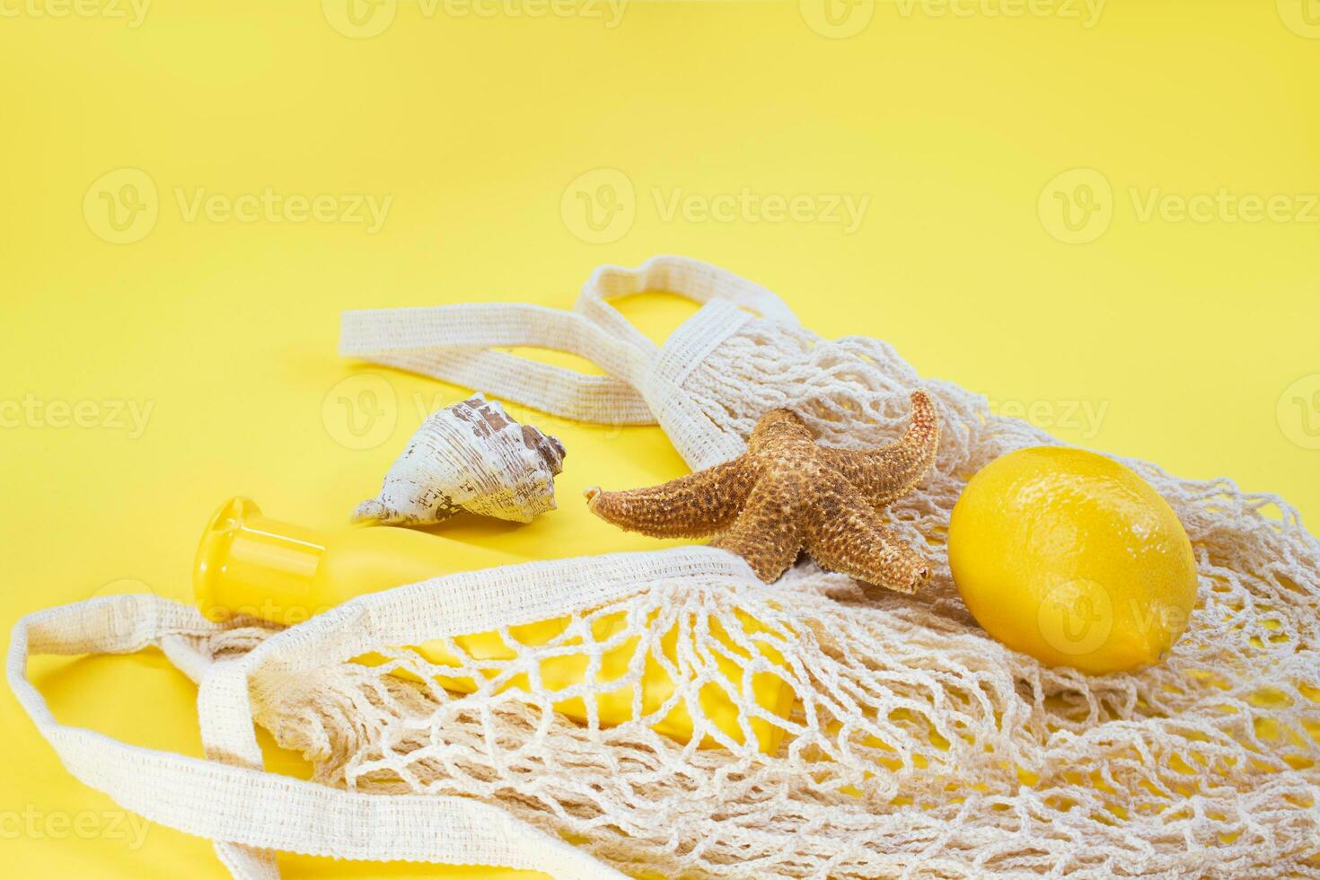 Starfish, shells with bag string with sunscreen bottle mockup and lemon from the side on yellow background. Concept of summer time, vacation, travel. Banner. Copy space photo