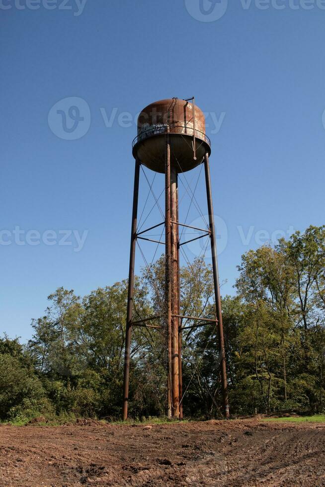 un hermosa agua torre es conjunto alrededor un abandonado área. esta oxidado metal estructura soportes alto en contra un azul cielo. foto
