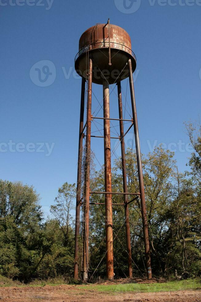 un hermosa agua torre es conjunto alrededor un abandonado área. esta oxidado metal estructura soportes alto en contra un azul cielo. foto