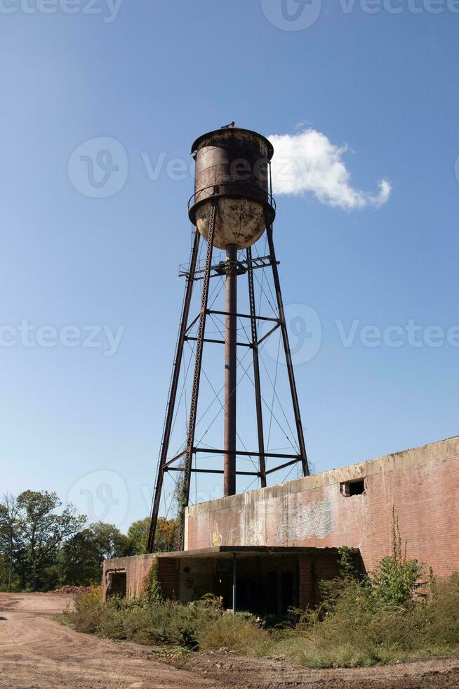 un hermosa agua torre es conjunto alrededor un abandonado área. esta oxidado metal estructura soportes alto en contra un azul cielo. foto