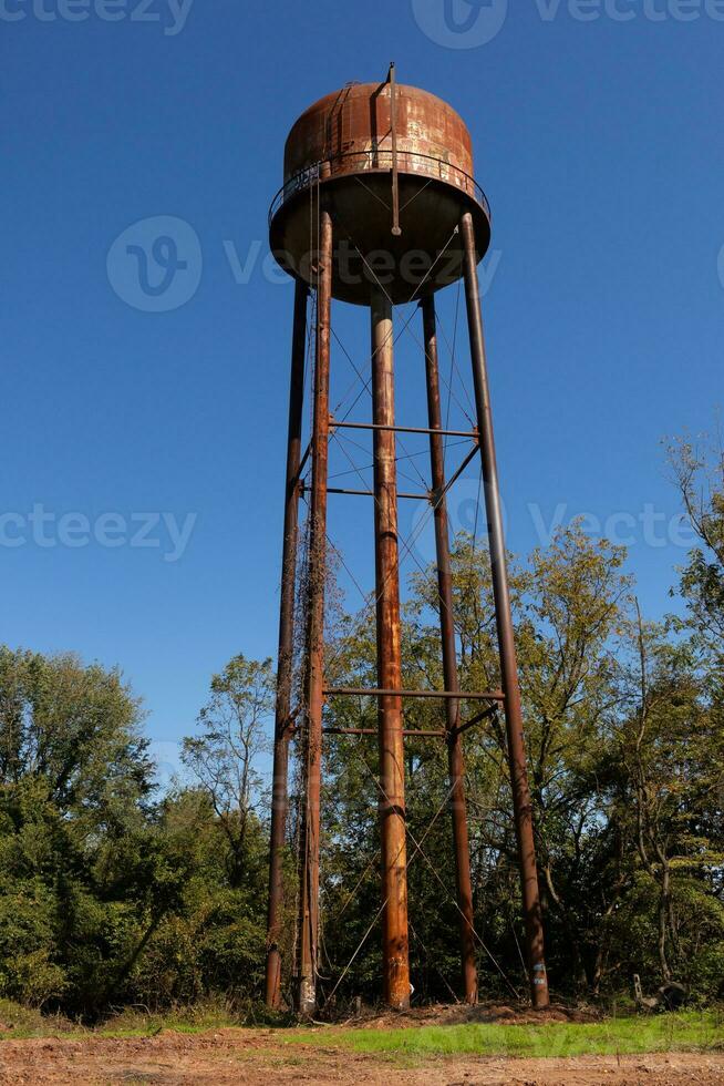 un hermosa agua torre es conjunto alrededor un abandonado área. esta oxidado metal estructura soportes alto en contra un azul cielo. foto