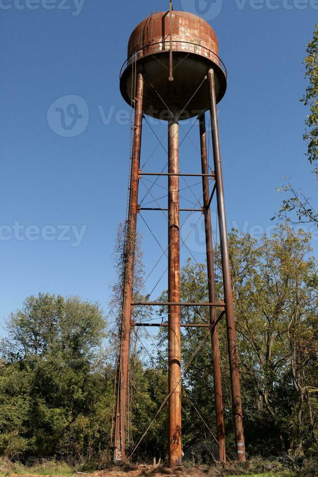 un hermosa agua torre es conjunto alrededor un abandonado área. esta oxidado metal estructura soportes alto en contra un azul cielo. foto