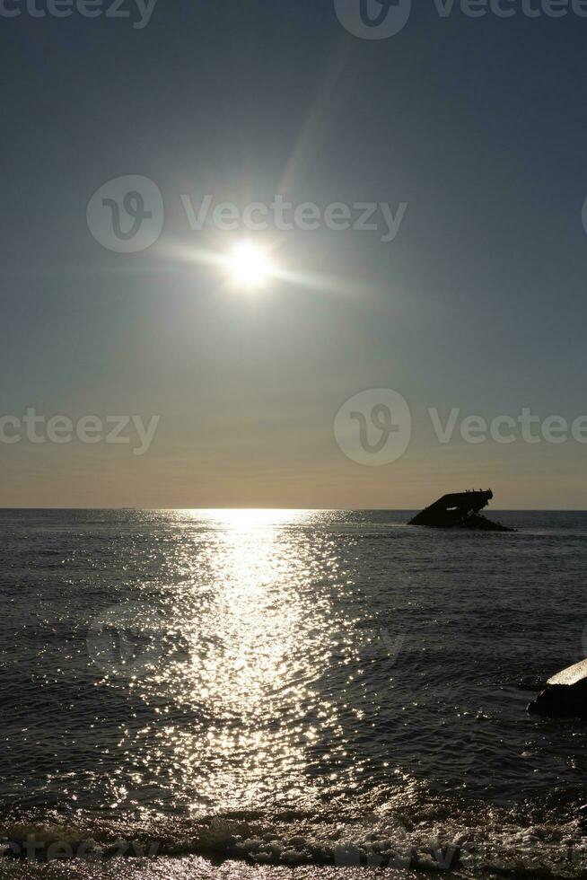 Sunset beach in Cape May New Jersey where you can get a great view of the sun going down across the ocean and the bay. The reflection of the sun on the water with the sunken ship looks so beautiful. photo