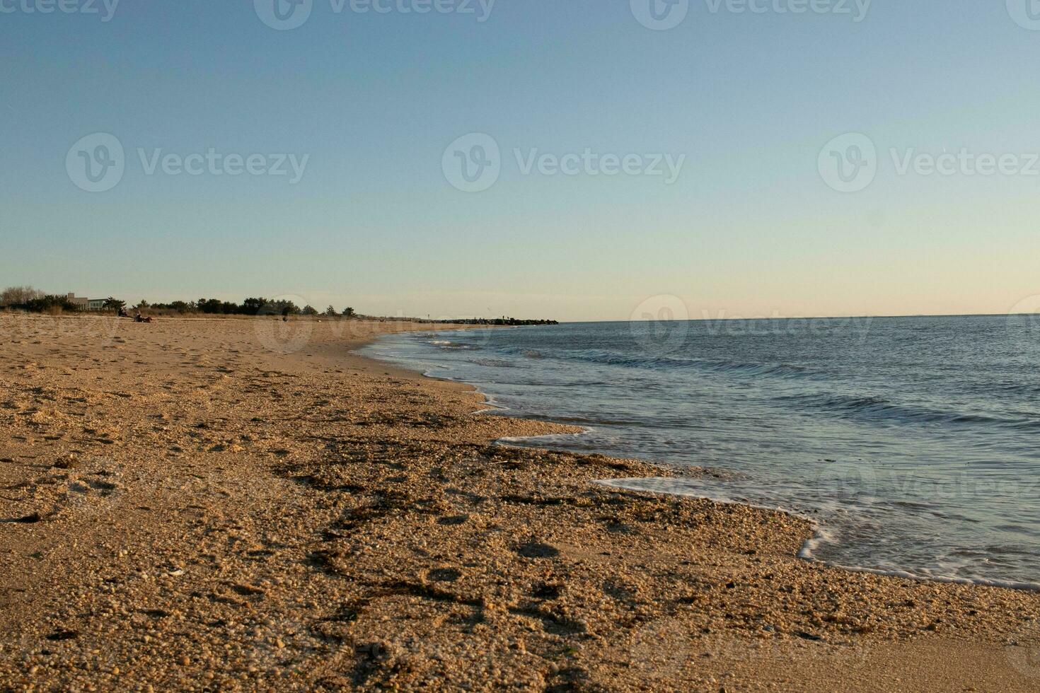 Pretty look of this beach as the waves came in to the shore. The water looking calm and the sand a golden brown. The beautiful sky with no clouds in site makes this look like a beautiful summer day. photo