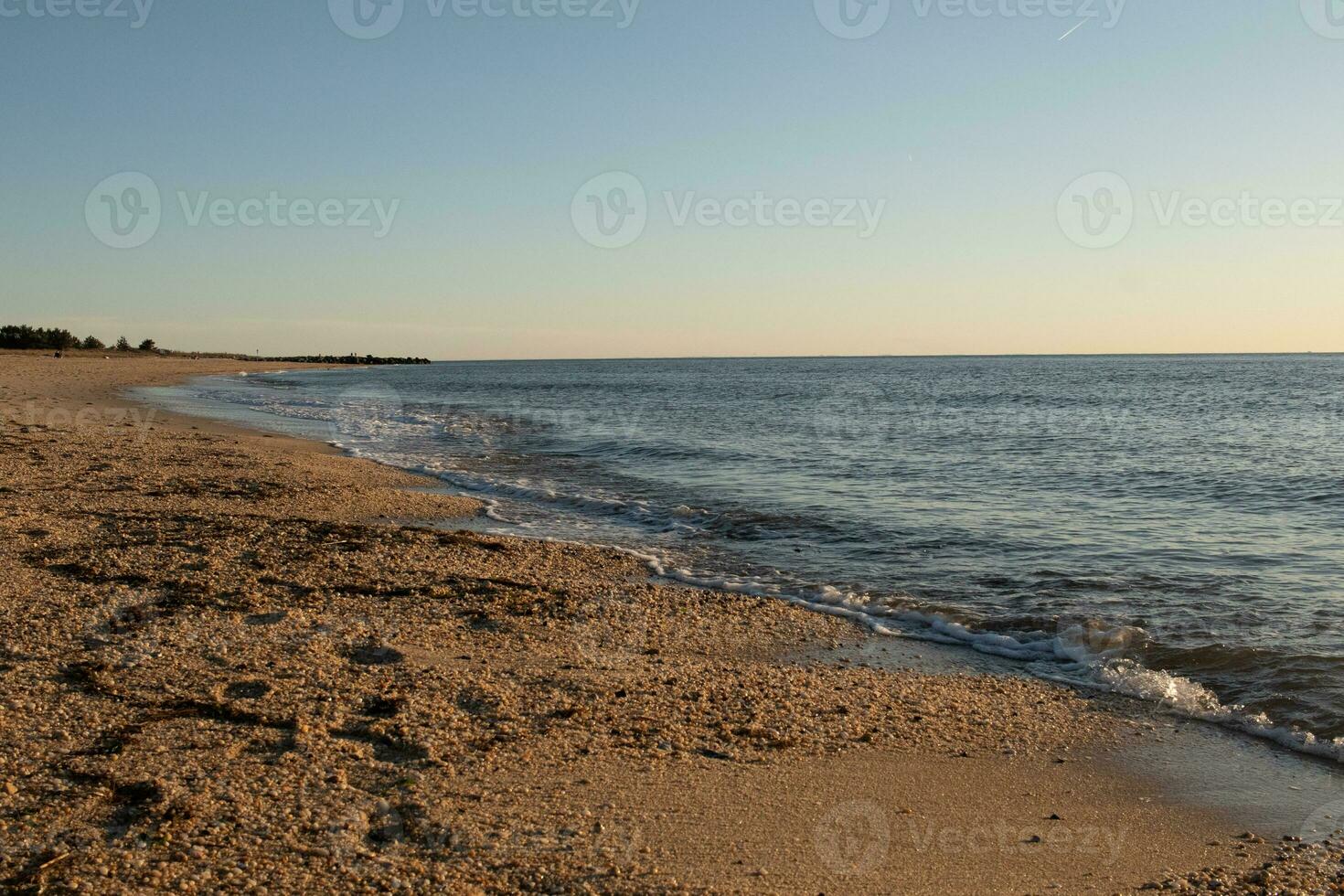 Pretty look of this beach as the waves came in to the shore. The water looking calm and the sand a golden brown. The beautiful sky with no clouds in site makes this look like a beautiful summer day. photo