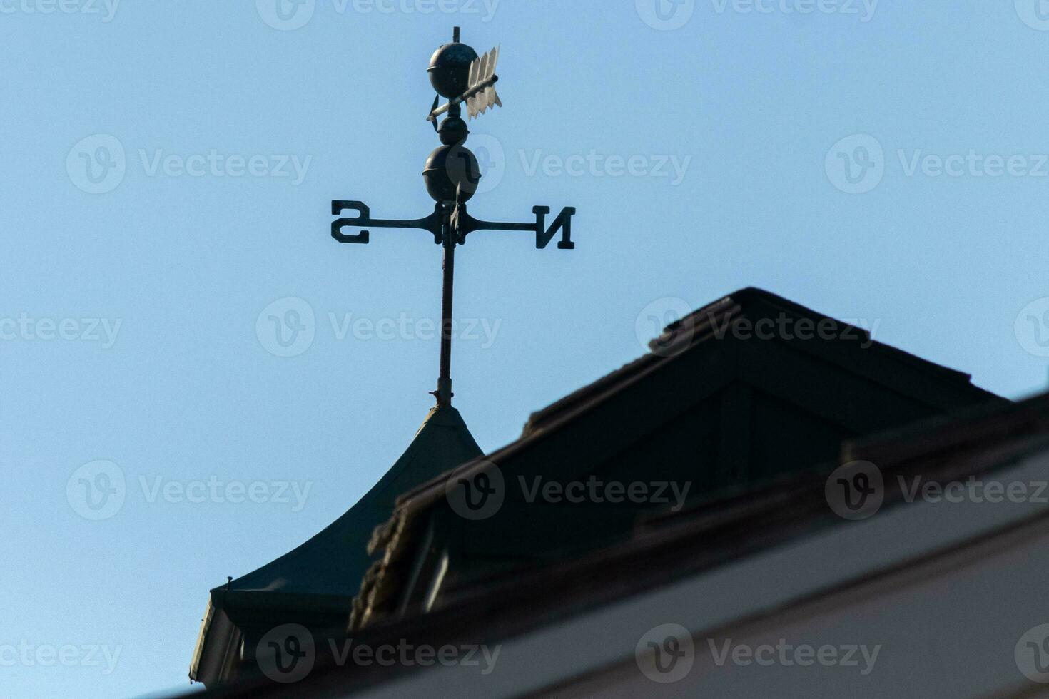 This weather vane was beautiful on the roof contrasted against the sky. The shadowy image with the clear blue sky in the background. The North, South, East, and West showing direction of the wind. photo