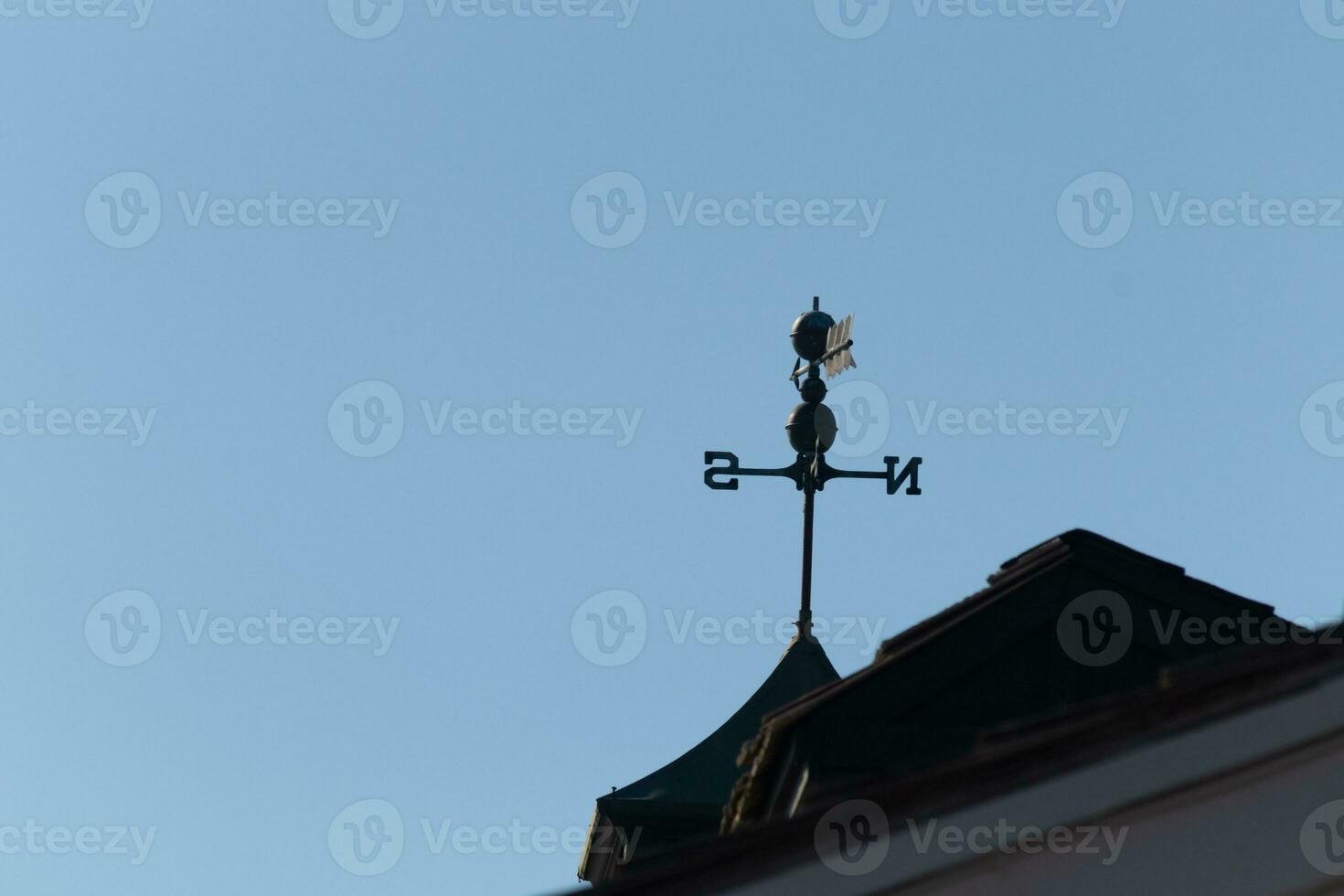 This weather vane was beautiful on the roof contrasted against the sky. The shadowy image with the clear blue sky in the background. The North, South, East, and West showing direction of the wind. photo